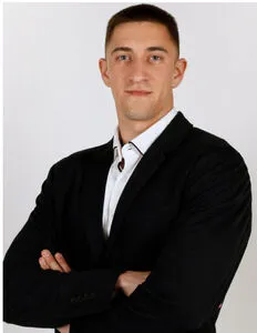 Modrá minimalistická ikona domečku s lupou, skrze lupu je vidět symbol dolaru.