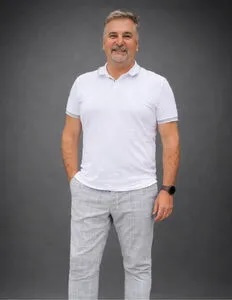 Modrá minimalistická ikona domečku s lupou, skrze lupu je vidět symbol dolaru.