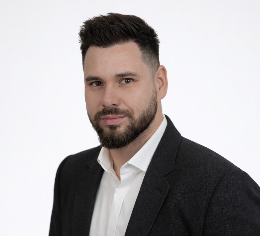 Modrá minimalistická ikona domečku s lupou, skrze lupu je vidět symbol dolaru.