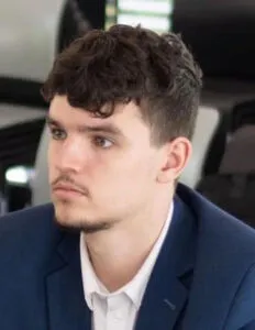 Modrá minimalistická ikona domečku s lupou, skrze lupu je vidět symbol dolaru.