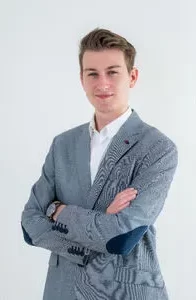 Modrá minimalistická ikona domečku s lupou, skrze lupu je vidět symbol dolaru.