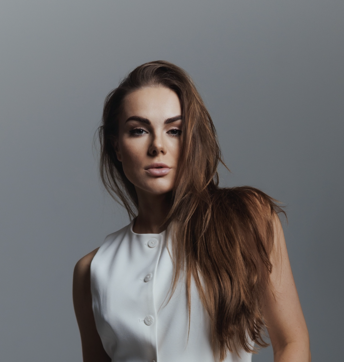 Modrá minimalistická ikona domečku s lupou, skrze lupu je vidět symbol dolaru.