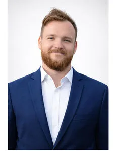 Modrá minimalistická ikona domečku s lupou, skrze lupu je vidět symbol dolaru.